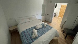 Une chambre à coucher comprenant un lit, une table de chevet, une chaise et une porte donnant sur une autre pièce.