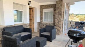 A covered outdoor seating area with wicker furniture and a barbecue grill. - Land. Beautiful apartment. Villa de Gredos (Barajas)