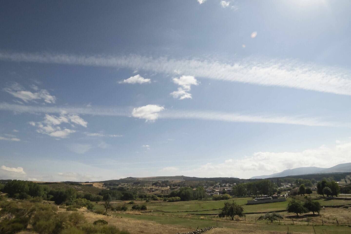 Paisaje rural con campos, árboles y colinas distantes bajo un cielo despejado.