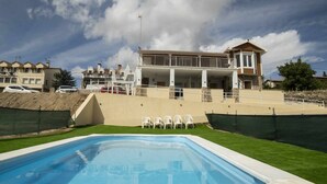 A swimming pool with a grassy area and white chairs, surrounded by a house with a balcony and a stone wall. - Land. Beautiful apartment. Villa de Gredos (Barajas)