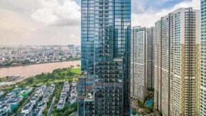 A high-rise building with a modern glass facade, surrounded by other high-rise buildings and a river in the background. - Vinhomes Central Park - PHAN DANG Residences (Ho Chi Minh City)
