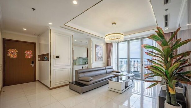 A modern living room with a sofa, coffee table, and a large plant. - Vinhomes Central Park - PHAN DANG Residences (Ho Chi Minh City)