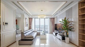 A modern living room with a sofa, TV, and a large plant. - Vinhomes Central Park - PHAN DANG Residences (Ho Chi Minh City)