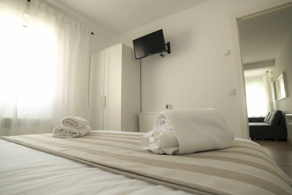 A hotel room with a bed, a flat-screen TV mounted on the wall, and a folded towel on the bed.