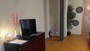 Uma sala de estar com um armário de madeira escura, uma televisão de tela plana, um vaso decorativo e um vaso de planta.