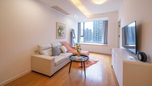 Un salon moderne avec un canapé, une table basse, un téléviseur et une fenêtre donnant sur la ville.