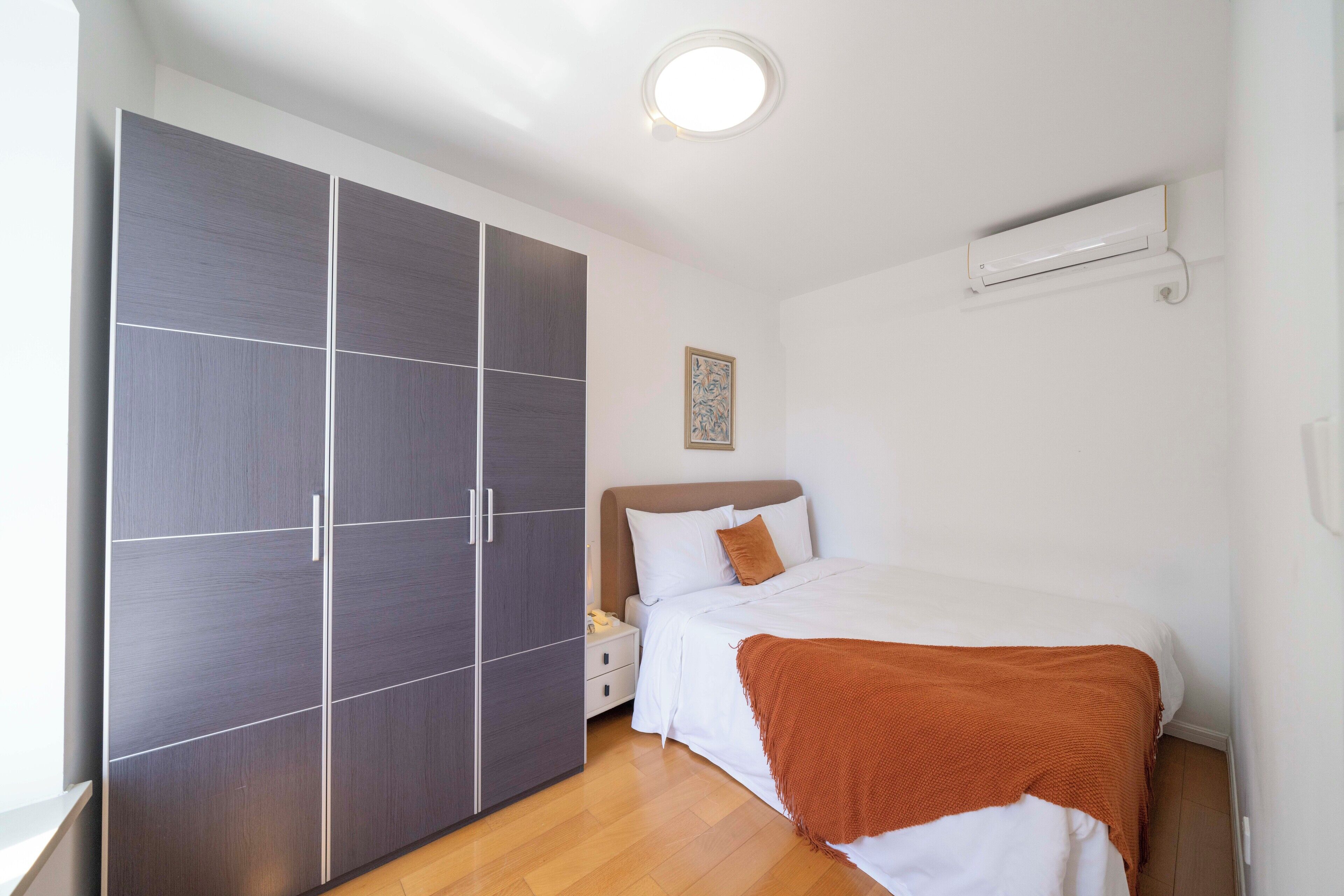A bedroom with a bed, a wardrobe, a nightstand, and a wall-mounted air conditioner.