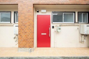 A red door with a metal handle, a brick wall, and a window above it. - sankennyahigasi101 (Osaka)