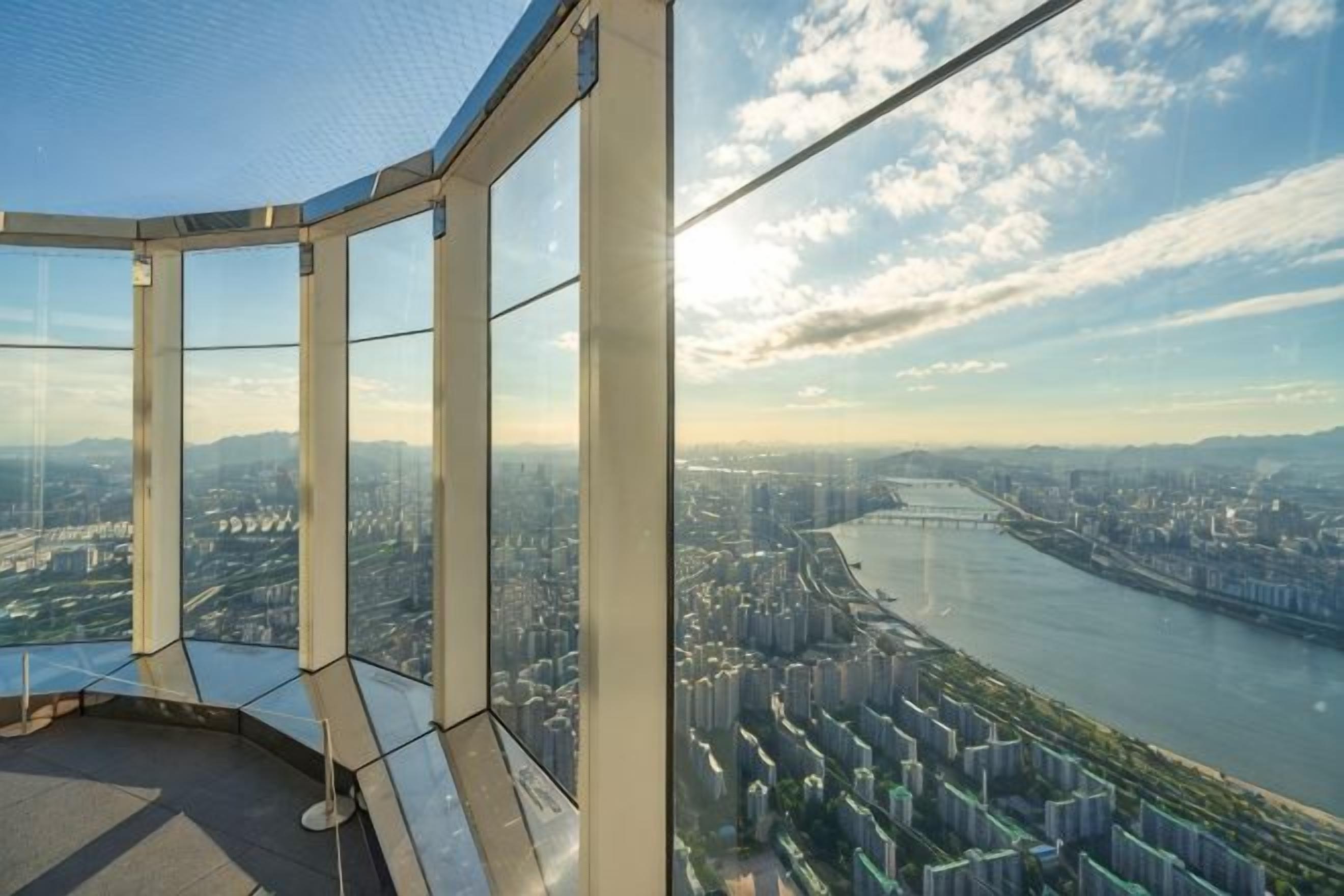 A panoramic view from a high-rise building with large windows, overlooking a cityscape and a river.