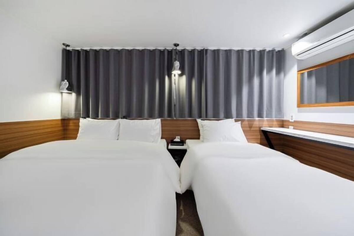 A hotel room with a large bed, a bedside table, a lamp, and a window with curtains.