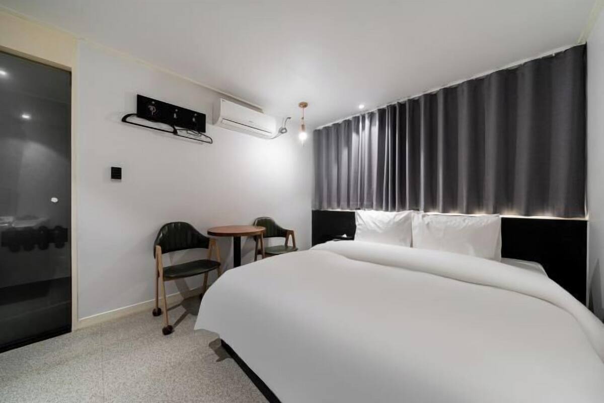 A hotel room with a large bed, a small table, two chairs, a headboard, and an air conditioning unit.