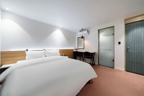 A hotel room with a large bed, a desk, and a chair. There is a mirror on the wall and a door with a handle. - Jamsil Noblestay Hotel (Seoul)