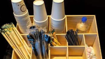 A wooden box containing stacks of white paper cups, plastic utensils, and a bottle of water.