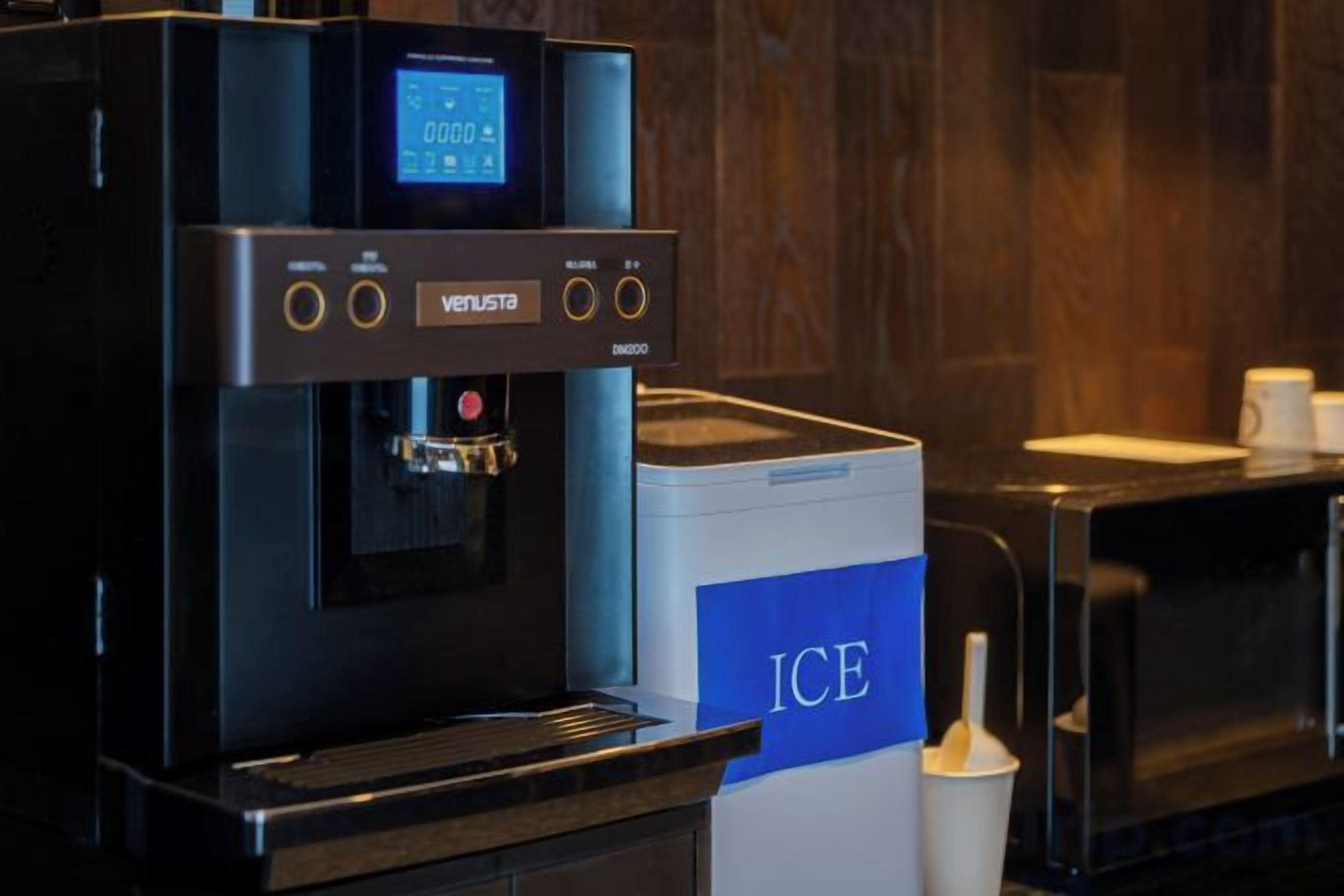 A coffee machine with a digital display, a microwave, and a box labeled 'ICE' on a counter.