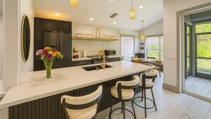 A modern kitchen with a large island, bar stools, and pendant lighting. - Horse Creek Retreat (Fort Myers)