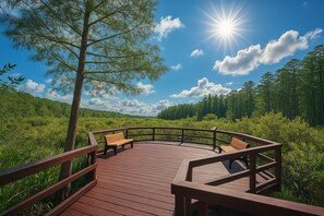 Een houten terras met banken, omringd door weelderige begroeiing en een heldere lucht.