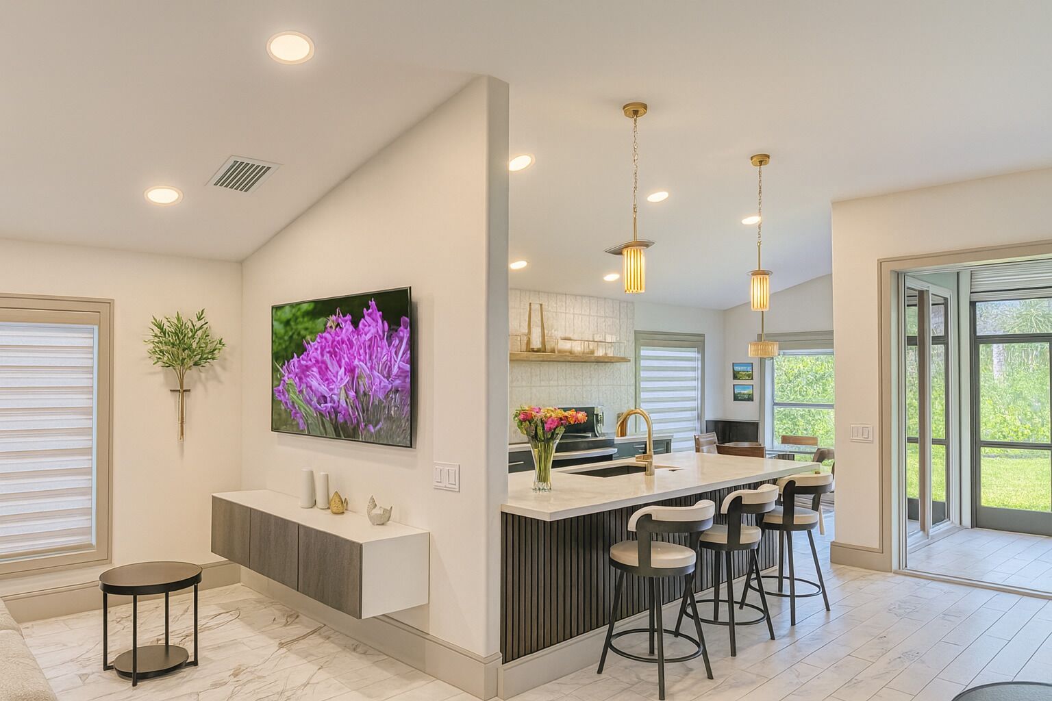 A modern kitchen with a central island, bar stools, pendant lighting, and a large window providing natural light.