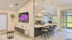 A modern kitchen with a central island, bar stools, pendant lighting, and a large window providing natural light. - Horse Creek Retreat (Fort Myers)