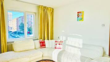 A living room with a sofa, a white armchair, and a window with curtains.