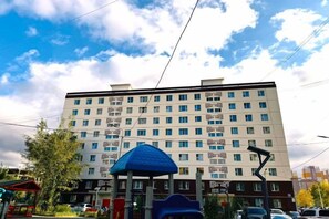 A multi-story building with a flat facade, several windows, and a blue structure in the foreground. - Apartment 44, spacious living area, separate kitchen & 1 bedroom (Ulaanbaatar)