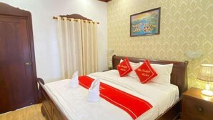 A hotel room with a bed, curtains, a painting, and a nightstand.
