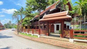 A traditional wooden building with a covered porch, palm trees, and a paved road.