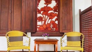 A room with two wicker chairs, a small wooden table, and a decorative panel with floral carvings.