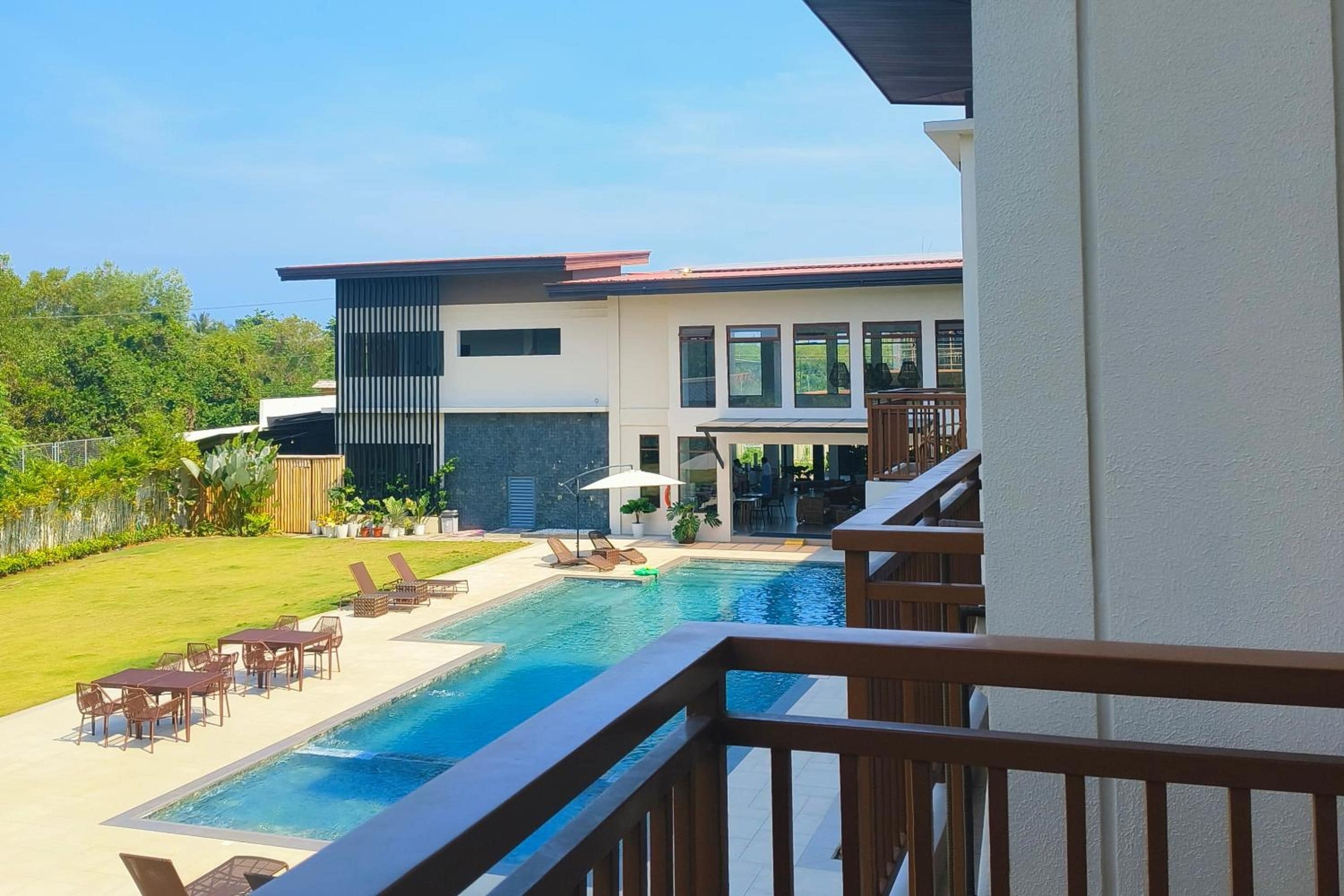 A modern building with a pool, outdoor seating, and a view of the surrounding greenery.