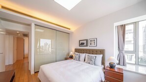A modern bedroom with a large bed, a nightstand with a lamp, a wardrobe, and a window with curtains. - Tyms Elegant 2BR 1BA Apt Walk to Malls (Shanghai)