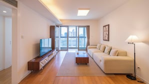 A modern living room with a sofa, coffee table, TV, and a city view through large windows. - Tyms Elegant 2BR 1BA Apt Walk to Malls (Shanghai)