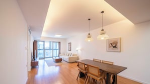 A spacious living area with a wooden dining table, a sofa, and a large window offering a view of the city. - Tyms Elegant 2BR 1BA Apt Walk to Malls (Shanghai)