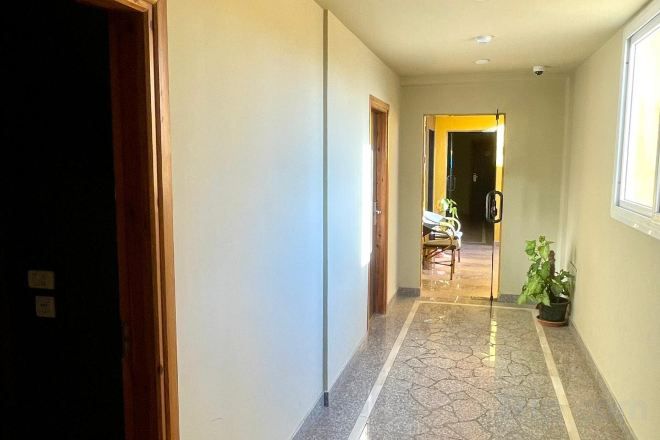 A hallway with a tiled floor, a door on the left, and a window on the right.
