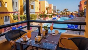 A balcony with a table set for two, overlooking a swimming pool and adjacent buildings. - Al Dora All Inclusive Hotel (Hurghada)