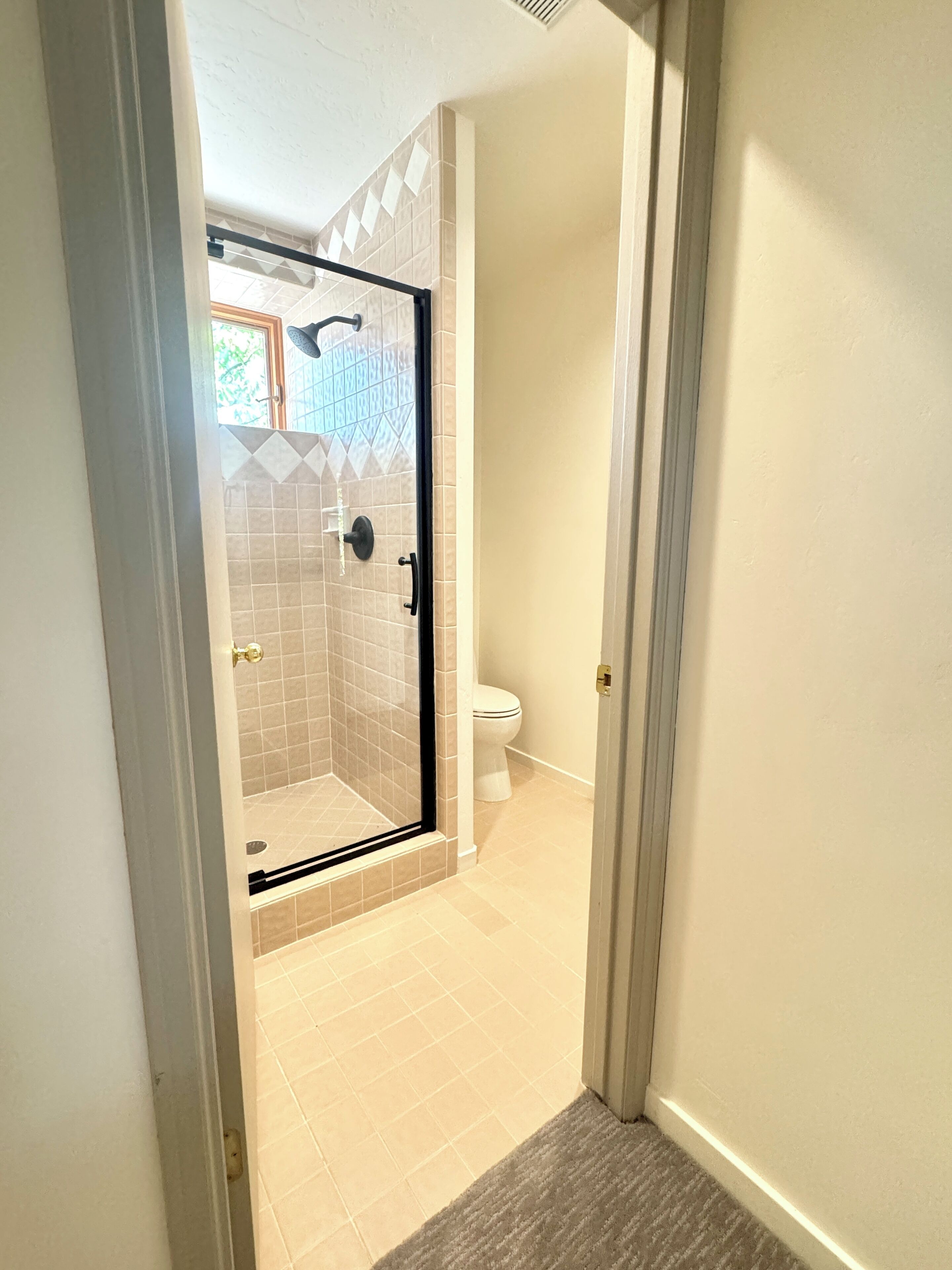 A bathroom with a glass-enclosed shower, a toilet, and a tiled floor.
