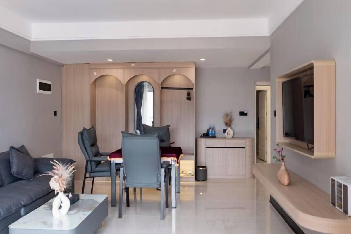 A modern living room with a sofa, chairs, a dining table, a TV, and a built-in kitchen area.