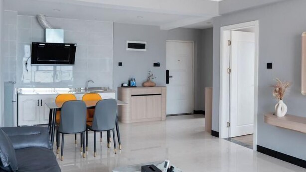 A modern living room with a sofa, a dining area with chairs, a kitchen with a TV, and a door leading to another room. - Starry Sky Resort Hotel (Boten)
