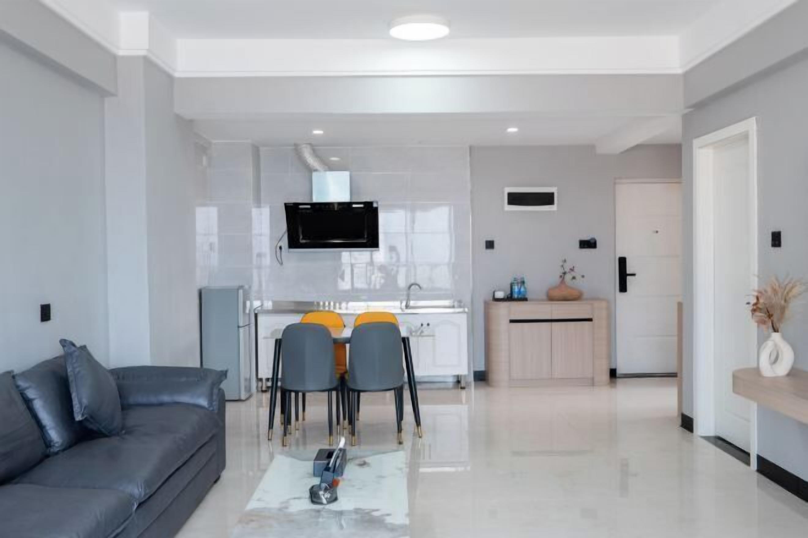 A modern living room with a grey sofa, a coffee table, and a dining area with chairs and a TV.