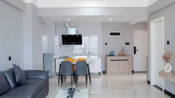 A modern living room with a grey sofa, a coffee table, and a dining area with chairs and a TV.