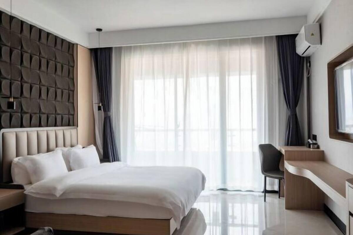 A modern hotel room with a large bed, a desk, and a view of the outdoors.