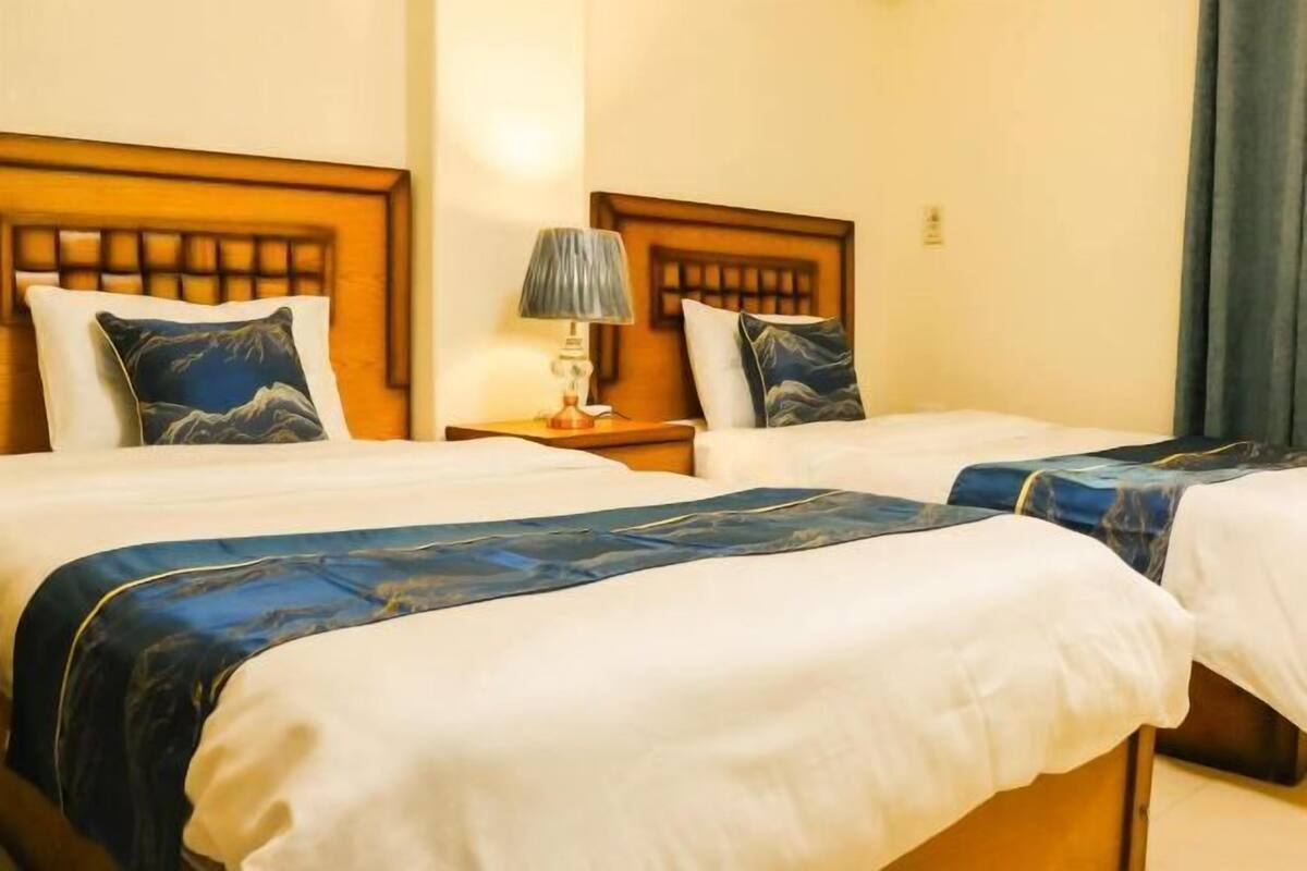 A hotel room with two beds, a nightstand with a lamp, and a view of the outside.