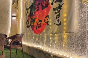 Un mur orné d’une grande banderole sur laquelle figurent des caractères chinois, une chaise en osier et des guirlandes lumineuses.