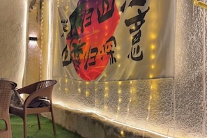 A room with a wall-mounted banner, a wicker chair, and a small green area. - Bafang Homestay (Cairo)