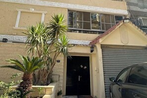 Un immeuble résidentiel avec un portail de garage, un palmier et une voiture garée.