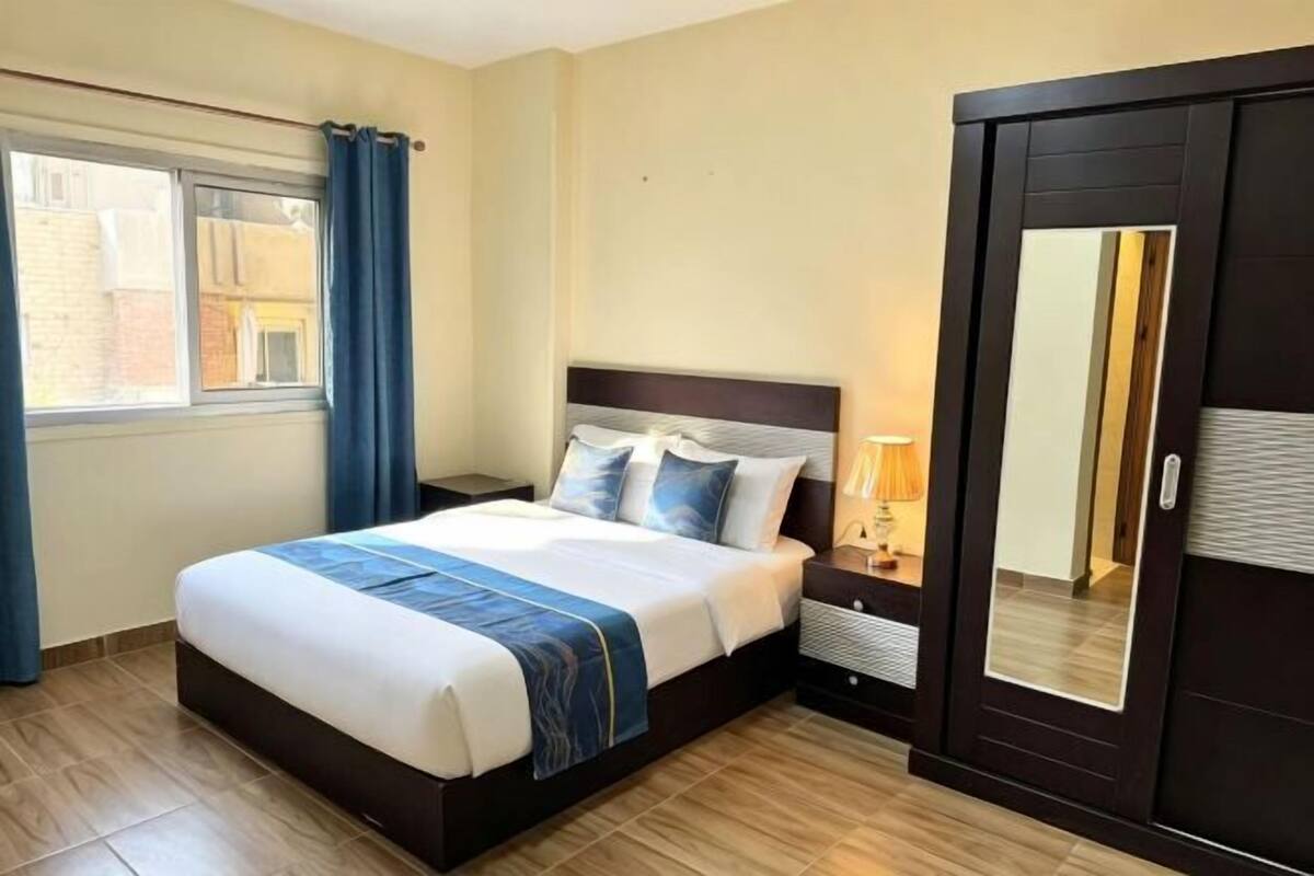 A hotel room with a bed, nightstand, lamp, and a wardrobe.
