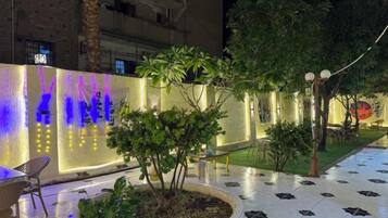 An outdoor area with a patterned floor, a well-lit wall with text, and a small tree in a planter.