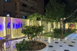 Un espace extérieur doté d’un sol à motifs, d’un mur bien éclairé sur lequel est inscrit un texte, et d’un petit arbre planté dans un pot.