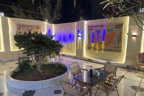 An outdoor seating area with a table and chairs, a small tree, and decorative lighting. - Bafang Homestay (Cairo)