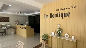 A reception area with a 'Welcome to Im Boutique' sign, a reception desk, a reception chair, and a reception counter with decorative items. - Imboutique hotel Maesot (Mae Sot)