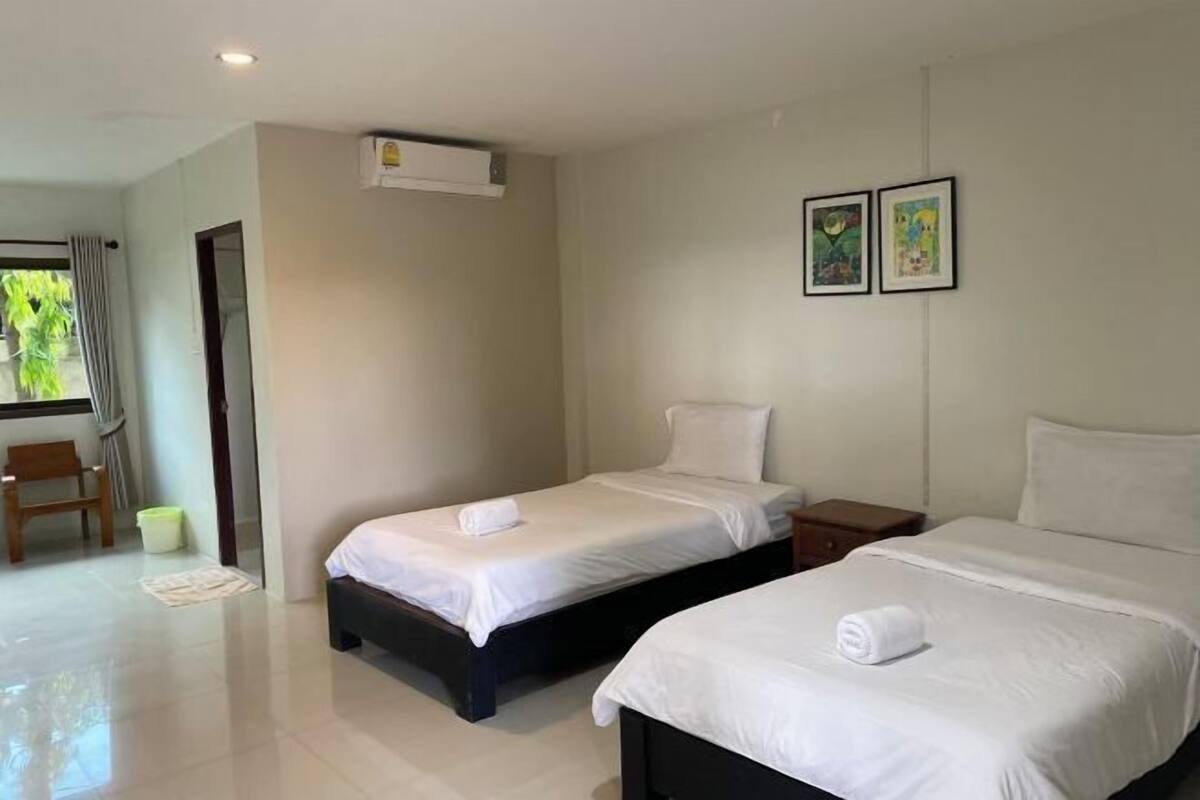 A hotel room with two beds, a small table, a chair, and a window with curtains.