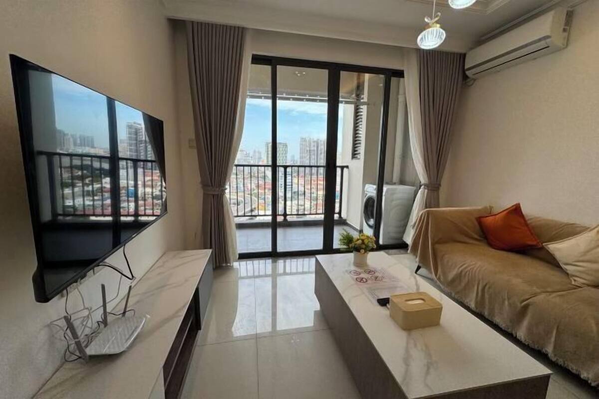 A modern living room with a large TV, a sofa, a coffee table, and a balcony with a city view.